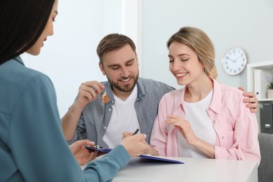 Photo of Happy young couple signing purchase contract in real estate agent's office. Man with new house key