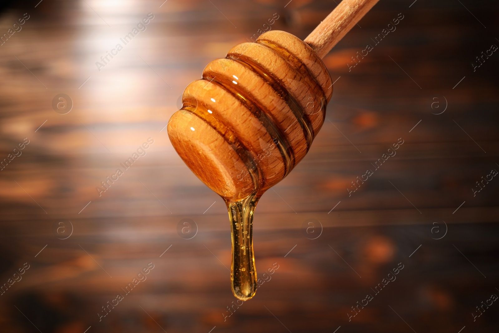 Photo of Dripping honey from wooden dipper on blurred background, closeup