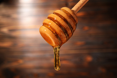 Photo of Dripping honey from wooden dipper on blurred background, closeup