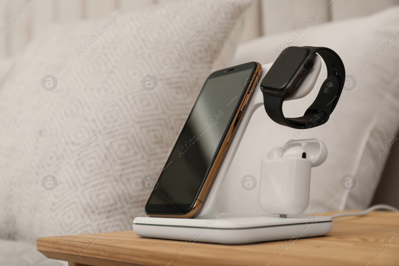 Photo of Different gadgets charging on wireless pad in bedroom, closeup