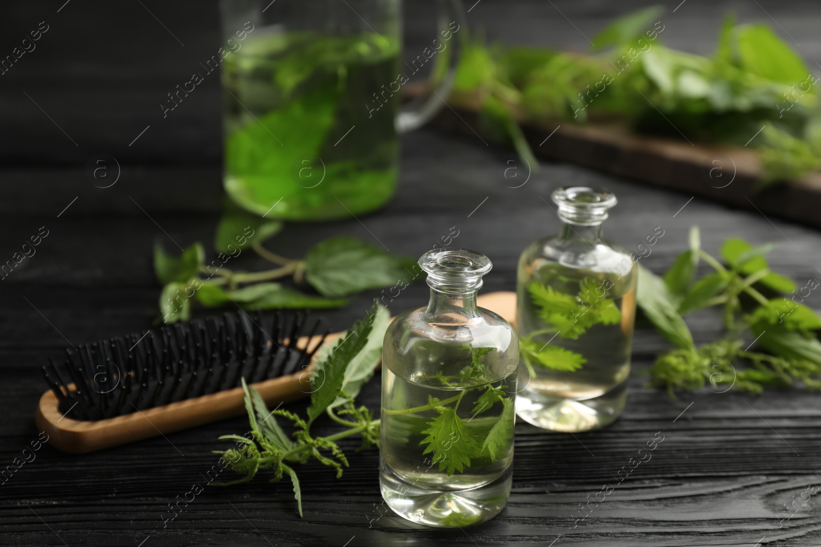 Photo of Stinging nettle, extract and brush on black wooden background. Natural hair care