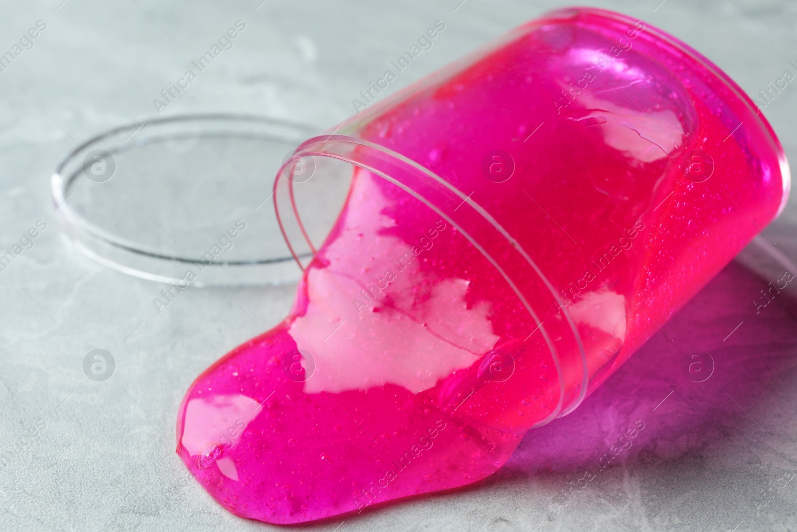 Photo of Overturned plastic container with pink slime on marble background, closeup
