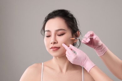 Woman getting facial injection on grey background