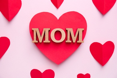 Photo of Beautiful composition with word MOM and paper hearts on color background. Happy Mother's Day