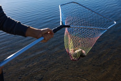 Photo of Fisherman holding fishing net with catch at riverside, closeup
