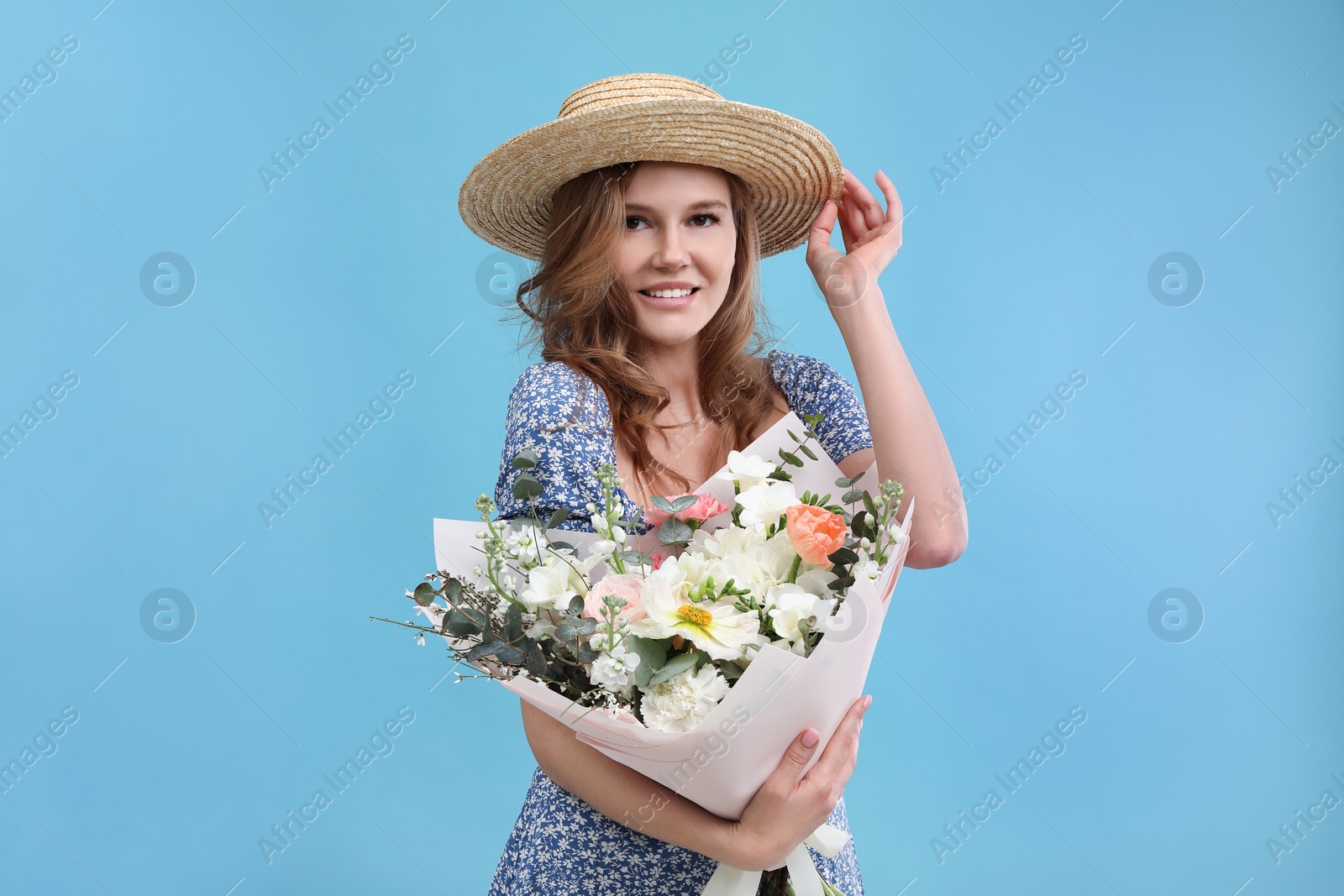 Photo of Beautiful woman in straw hat with bouquet of flowers on light blue background