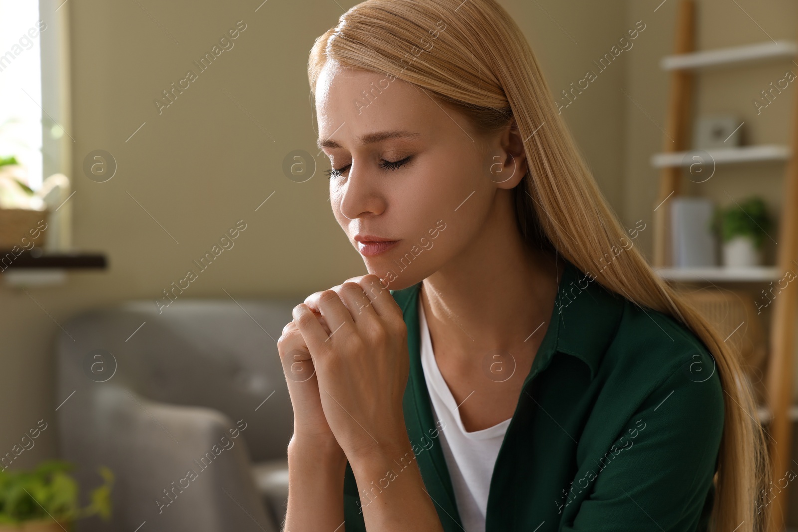 Photo of Religious young woman with clasped hands praying indoors