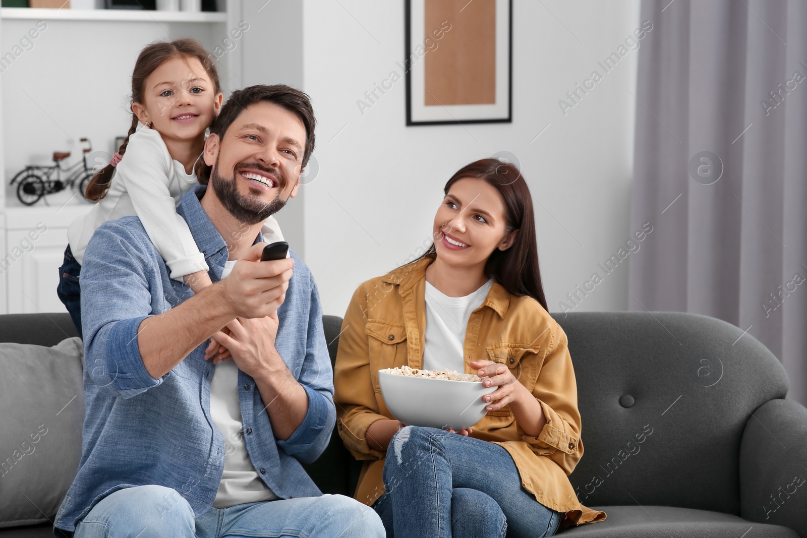 Photo of Happy family watching movie at home. Father changing TV channels with remote control