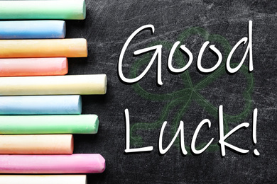 Image of Pieces of color chalk and phrase GOOD LUCK on blackboard, flat lay