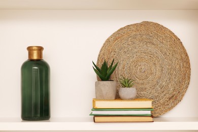 Photo of Shelf with houseplants, books and bottle near beige wall. Interior design