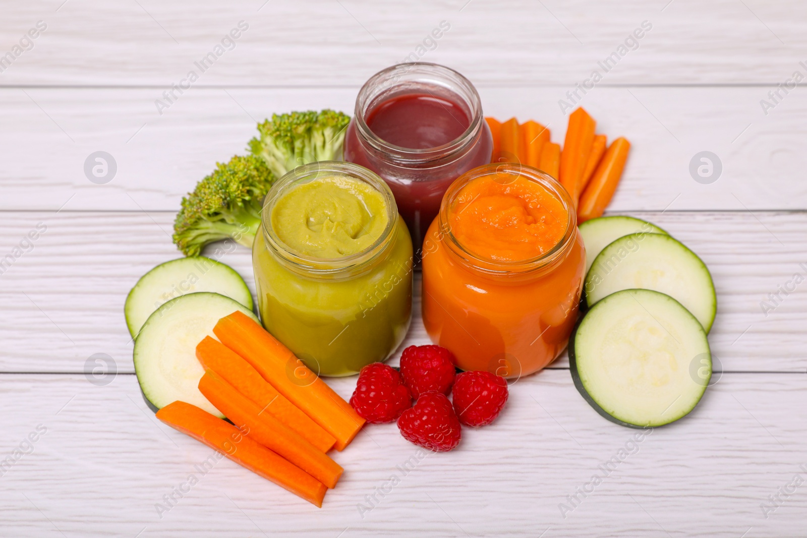 Photo of Jars with healthy baby food and ingredients on white wooden table