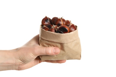 Photo of Woman holding paper bag with tasty roasted edible chestnuts on white background, closeup