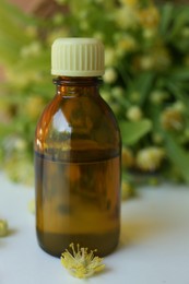 Photo of Bottle of essential oil and linden blossoms on white table, closeup