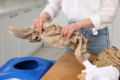 Photo of Woman separating garbage at wooden table indoors, closeup