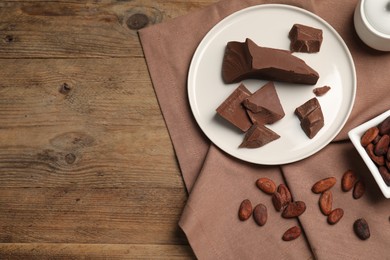 Photo of Pieces of tasty milk chocolate and cocoa beans on wooden table, top view. Space for text