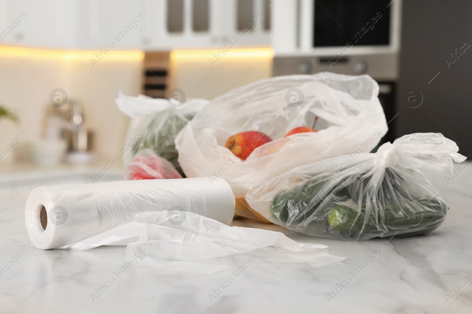 Photo of Plastic bags with different fresh products on white marble table in kitchen