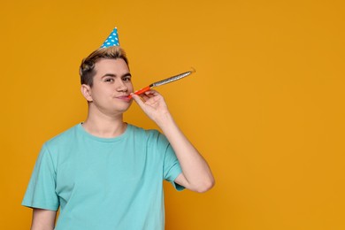 Photo of Young man with party hat and blower on orange background, space for text