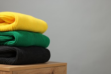 Photo of Stack of knitted sweaters on wooden table against grey background. Space for text