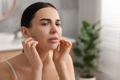 Woman with dry skin checking her face near mirror indoors, space for text