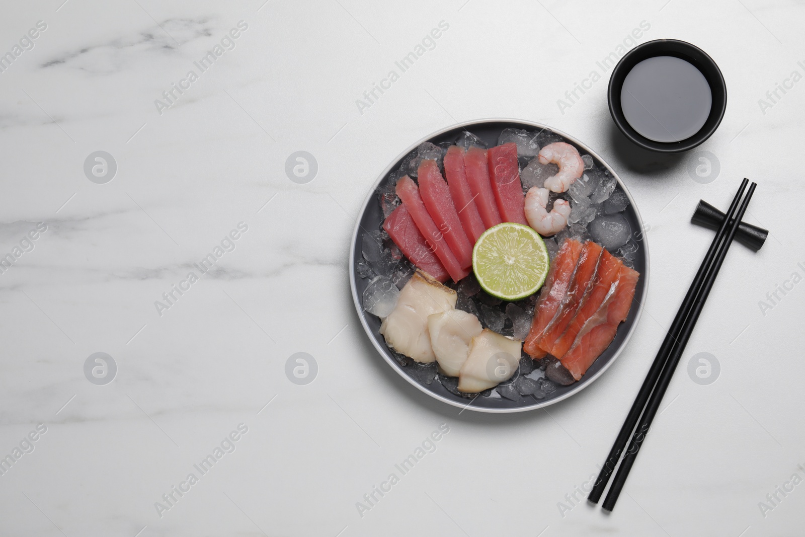 Photo of Sashimi set (raw slices of tuna, salmon, oily fish and shrimps) served with lime, soy sauce and ice on white marble table, flat lay. Space for text