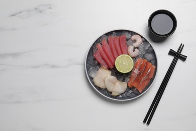 Photo of Sashimi set (raw slices of tuna, salmon, oily fish and shrimps) served with lime, soy sauce and ice on white marble table, flat lay. Space for text