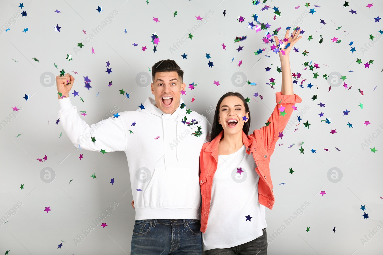 Photo of Happy couple and falling confetti on light grey background