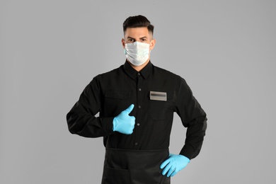 Photo of Waiter wearing medical face mask on light grey background