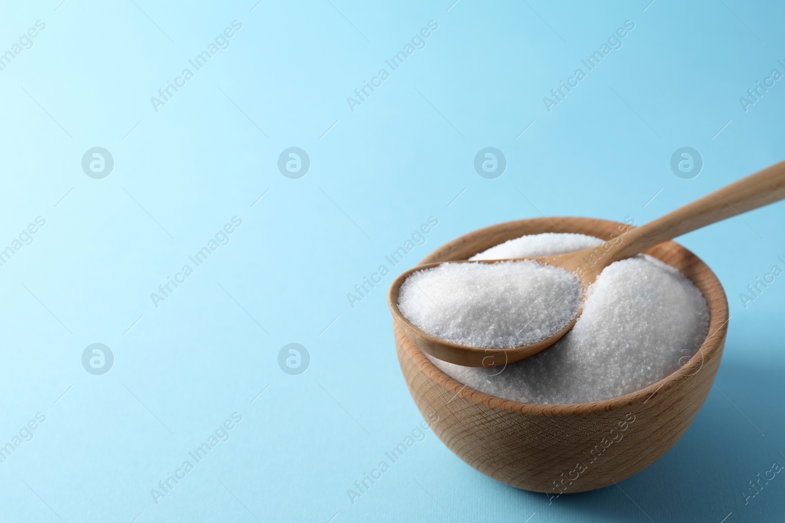 Photo of Organic white salt in bowl and spoon on light blue background, space for text