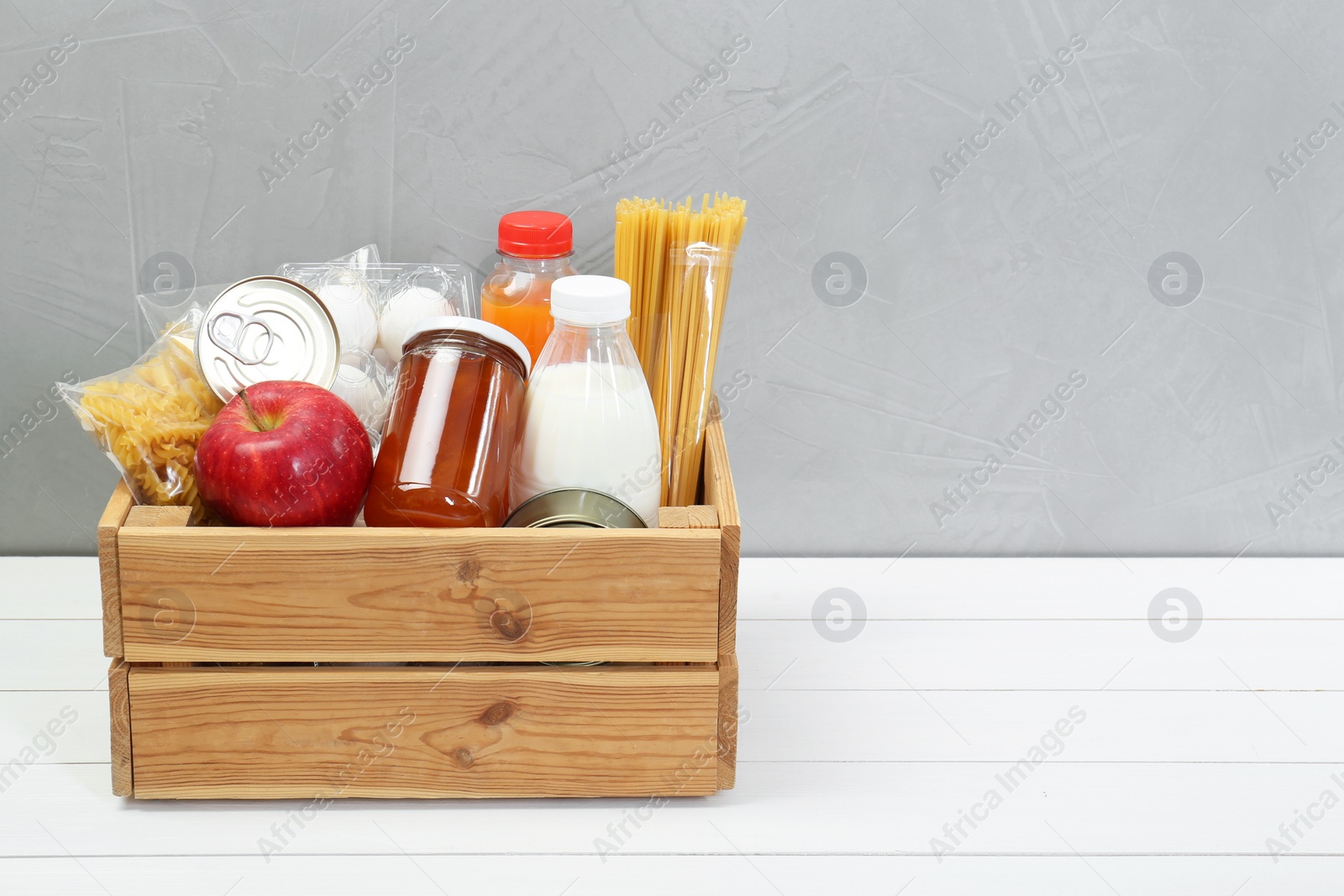 Photo of Humanitarian aid. Different food products for donation in crate on white wooden table. Space for text