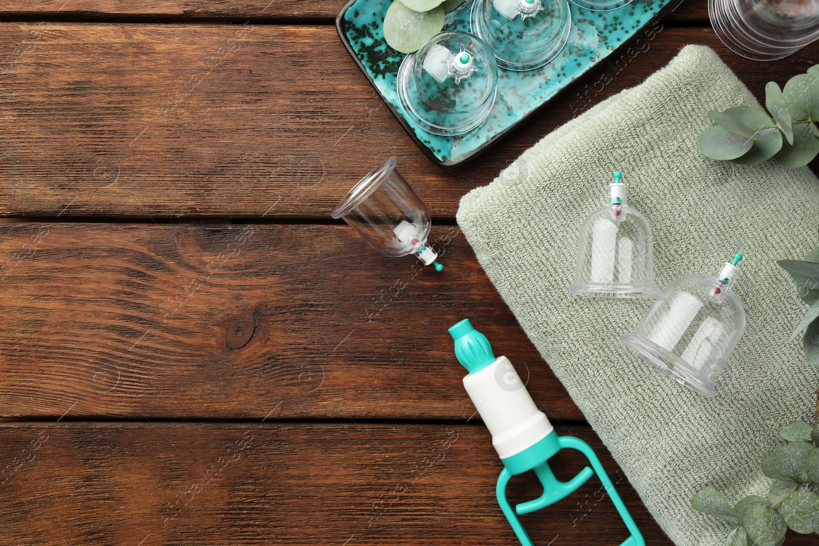 Photo of Cupping therapy. Plastic cups, hand pump, towel and eucalyptus leaves on wooden table, flat lay. Space for text