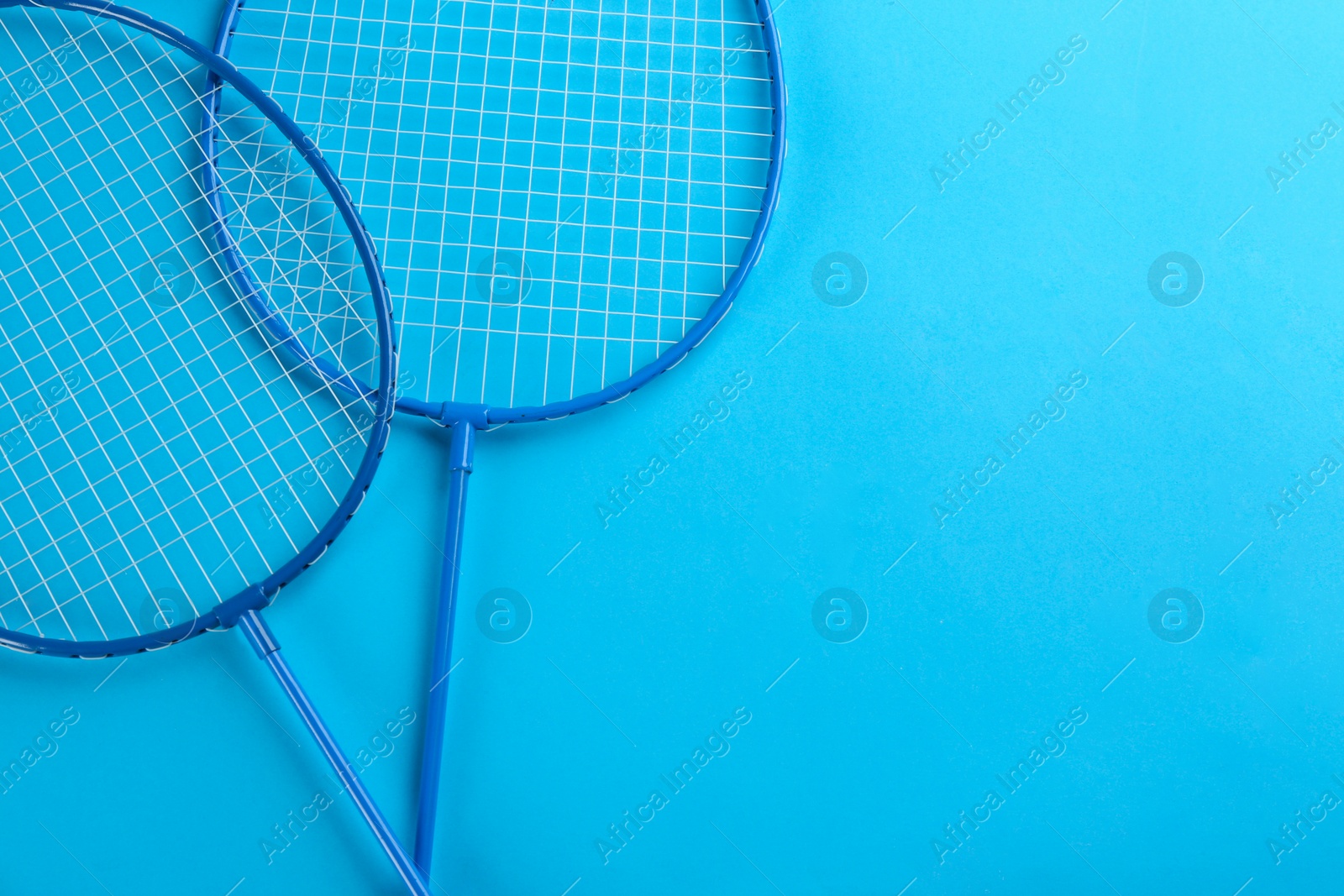 Photo of Badminton rackets on light blue background, flat lay. Space for text