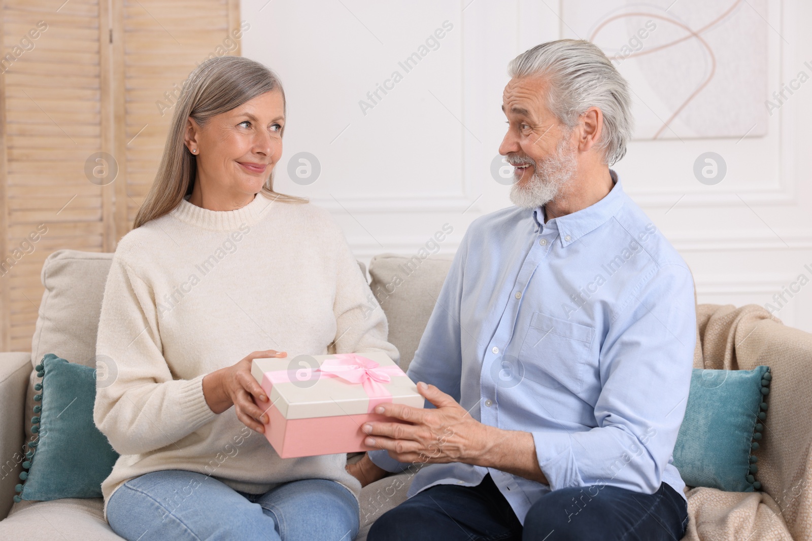 Photo of Happy affectionate senior couple with gift box on sofa indoors