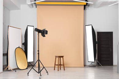 Photo of Beige photo background, stool and professional lighting equipment in studio