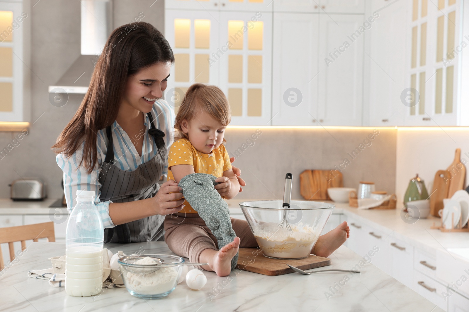 Photo of Mother and her little daughter cooking dough together in kitchen