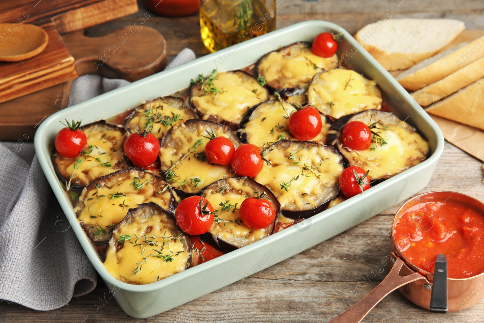 Photo of Baked eggplant with tomatoes and cheese in dishware on wooden table