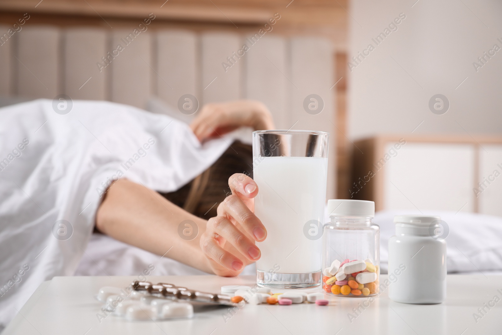Photo of Woman taking medicine for hangover in bed at home, focus on hand with glass