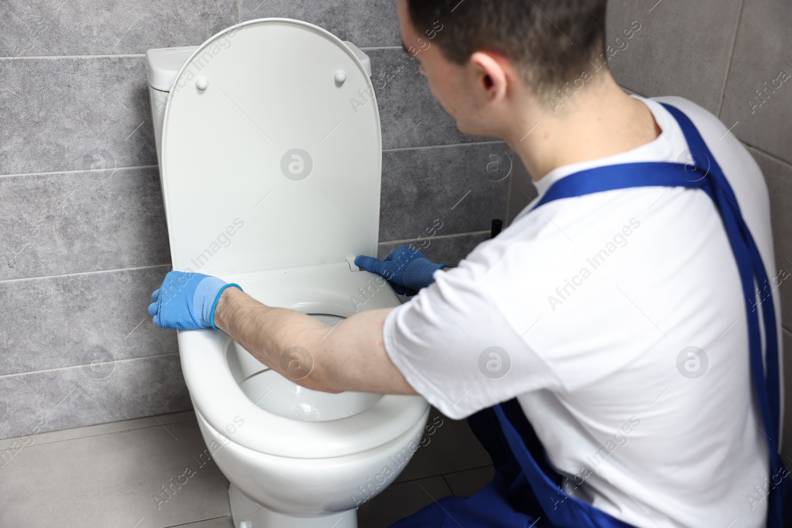 Photo of Young plumber wearing protective gloves repairing toilet bowl in water closet