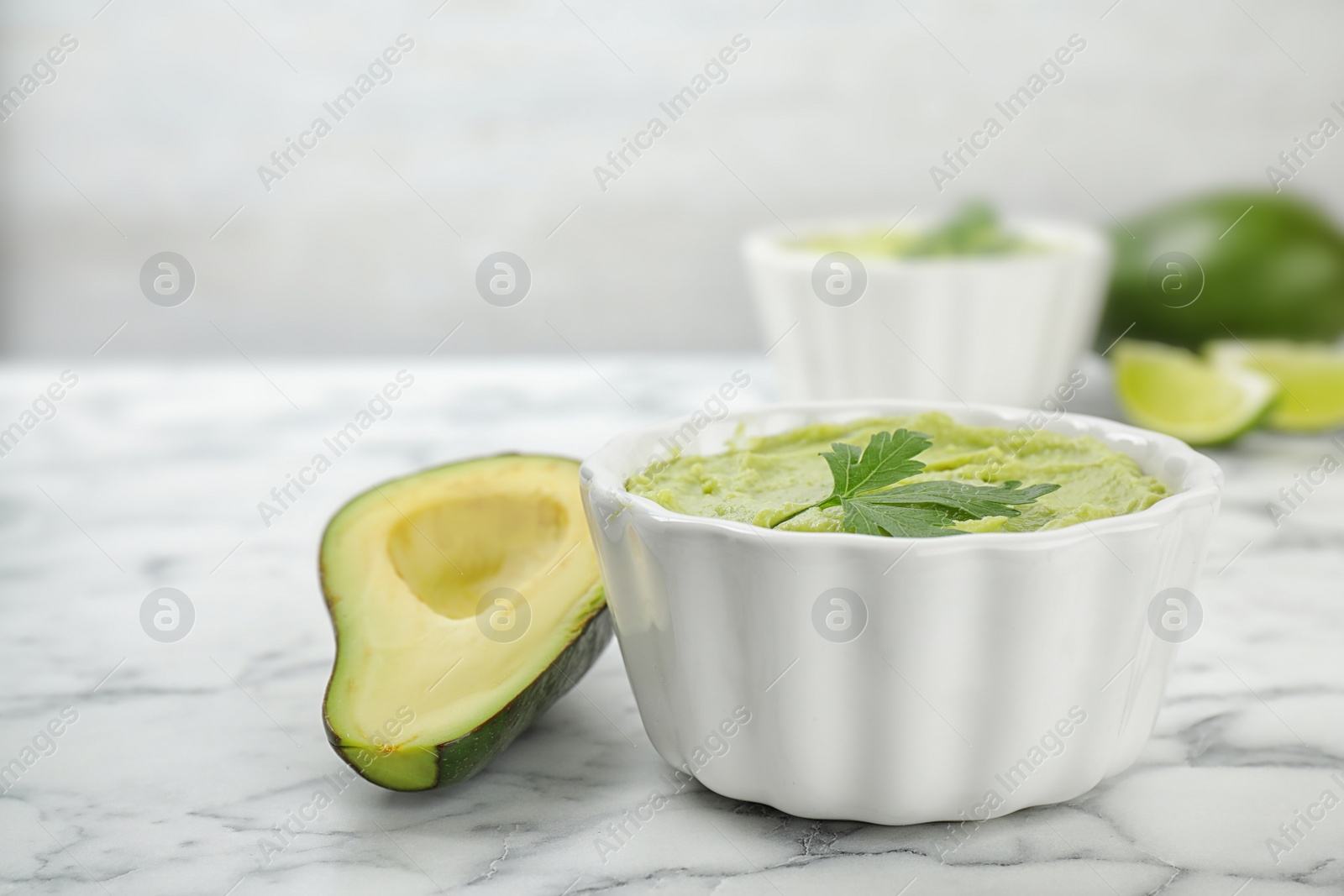 Photo of Bowl of guacamole with parsley and cut avocado on marble table