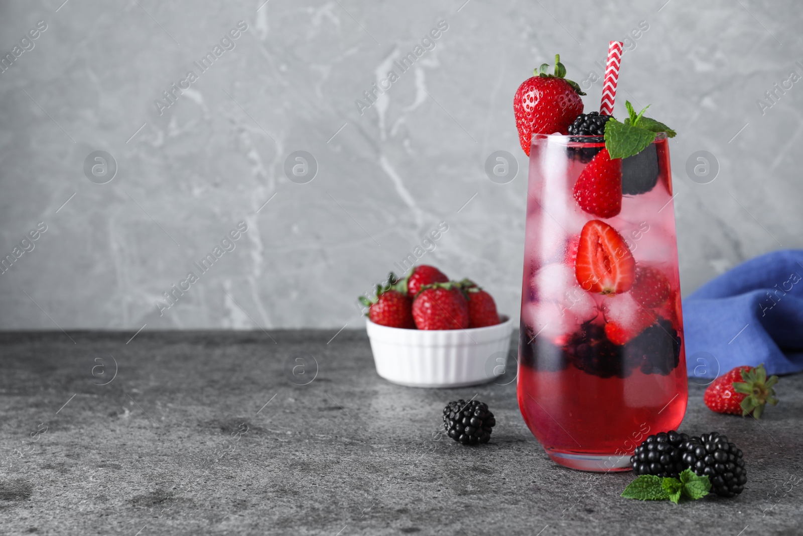 Photo of Delicious strawberry lemonade with soda water, mint and blackberries on grey table, space for text. Fresh summer cocktail