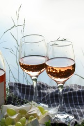 Photo of Delicious rose wine, cheese and grapes on picnic blanket near lake