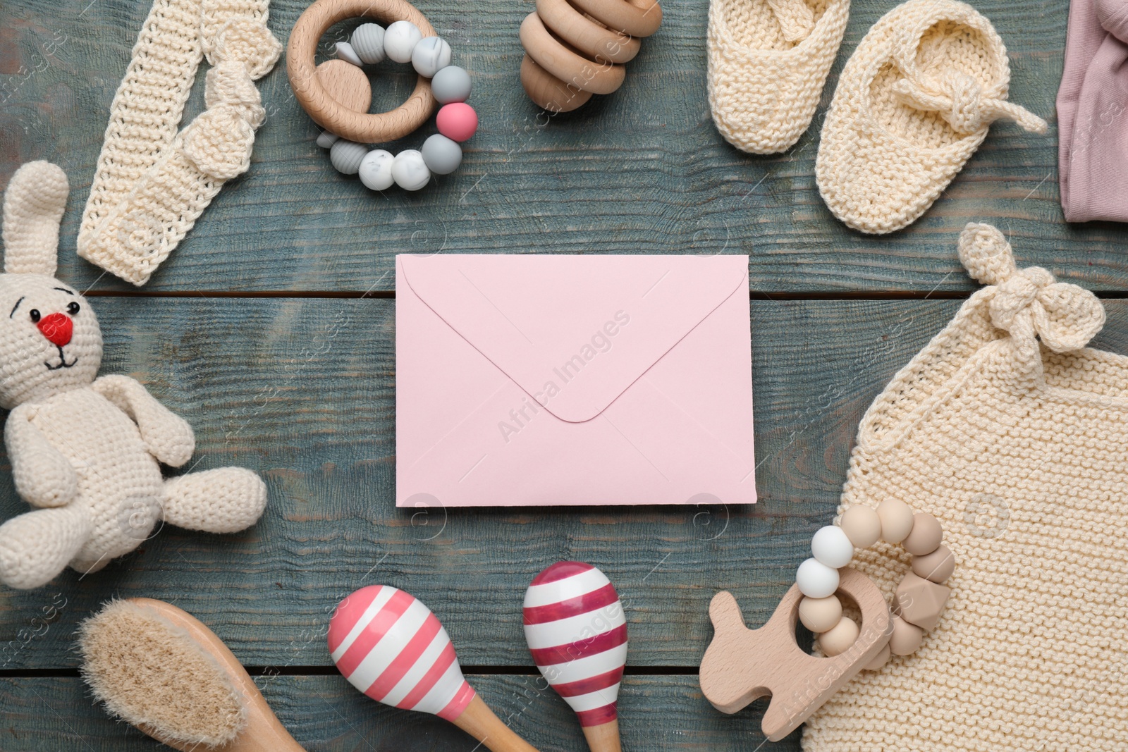 Photo of Baby shower party. Envelope surrounded by stuff for child on light blue wooden background, flat lay