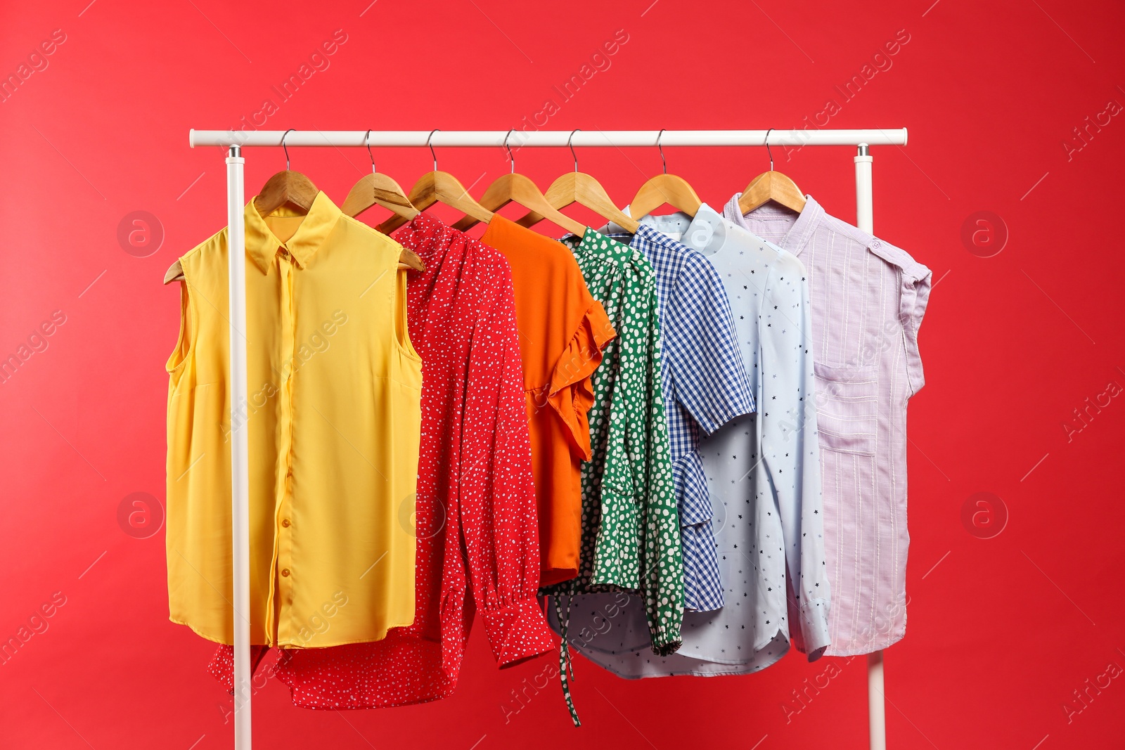 Photo of Bright clothes hanging on rack against red background. Rainbow colors