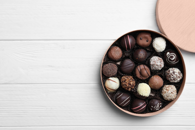 Photo of Box with tasty chocolate candies on white wooden table, flat lay. Space for text