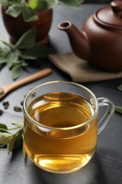 Photo of Cup of aromatic sage tea on black table. Space for text