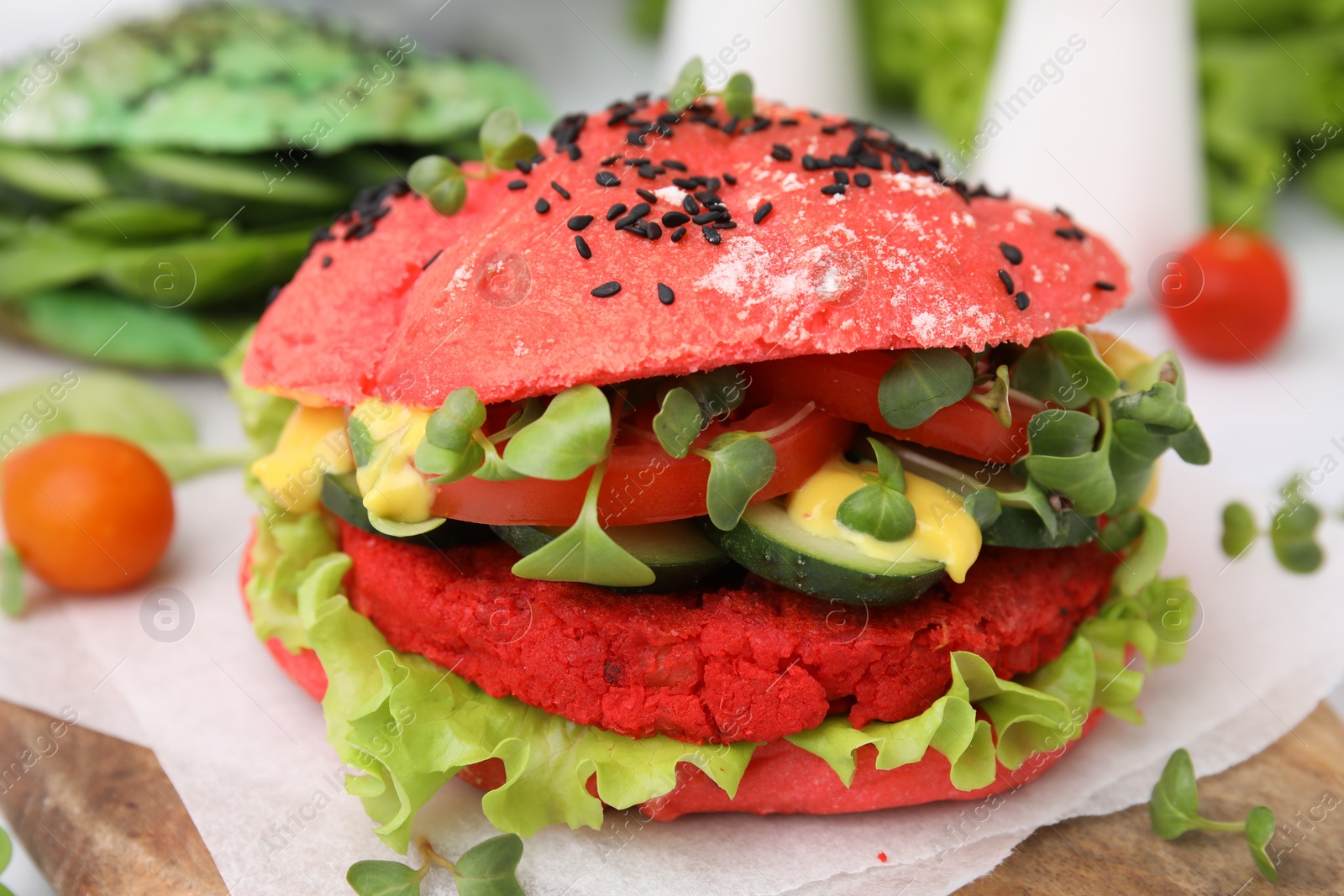 Photo of Tasty pink vegan burger with vegetables, patty and microgreens on wooden table, closeup