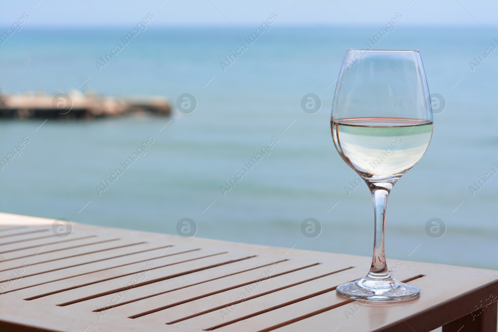 Photo of Glass with wine on table near sea. Space for text