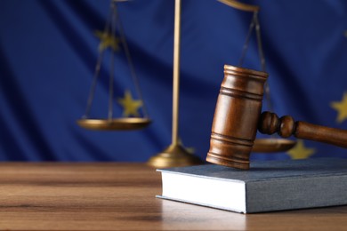 Judge's gavel and book on wooden table against European Union flag. Space for text