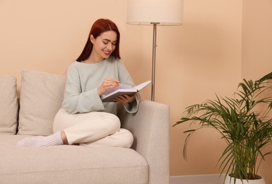 Photo of Happy woman with red dyed hair reading book at home