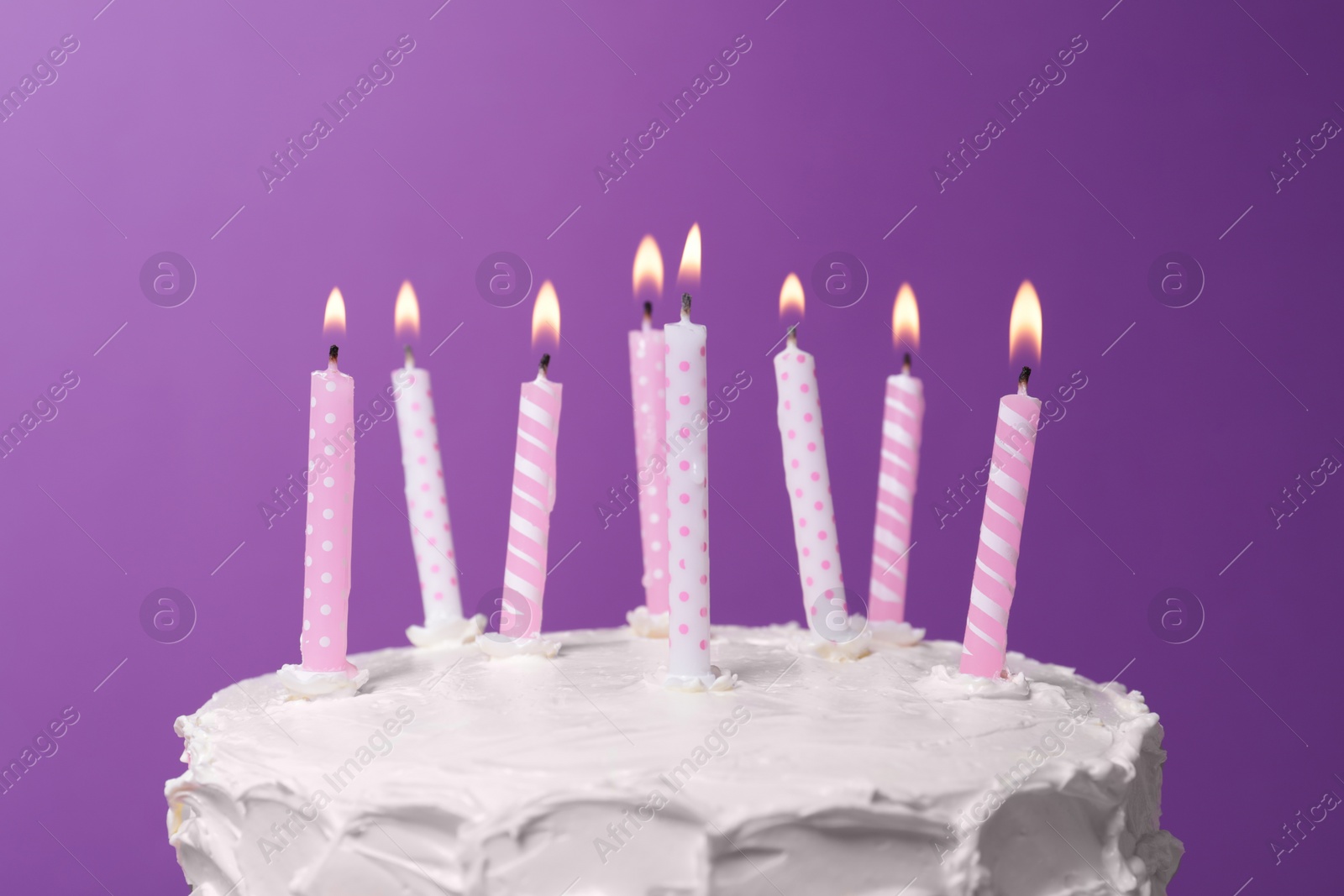 Photo of Delicious cake with cream and burning candles on purple background, closeup