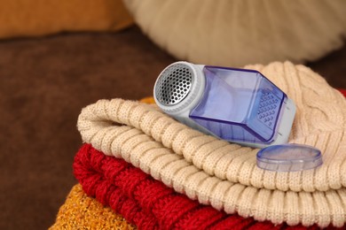 Photo of Modern fabric shaver and knitted clothes on brown background, closeup